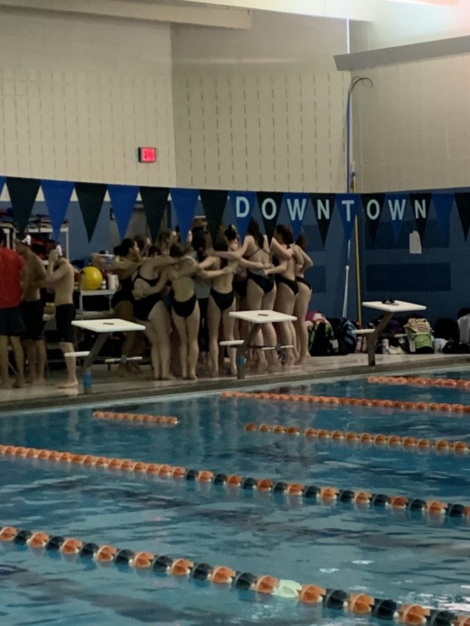 The members of the swim team being lead in a cheer before the first event to get them excited for the meet.