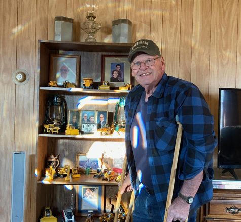 Mr. Bruce Pennington stands on crutches in front of his excavator collection, a testament to his 50 years working in construction.